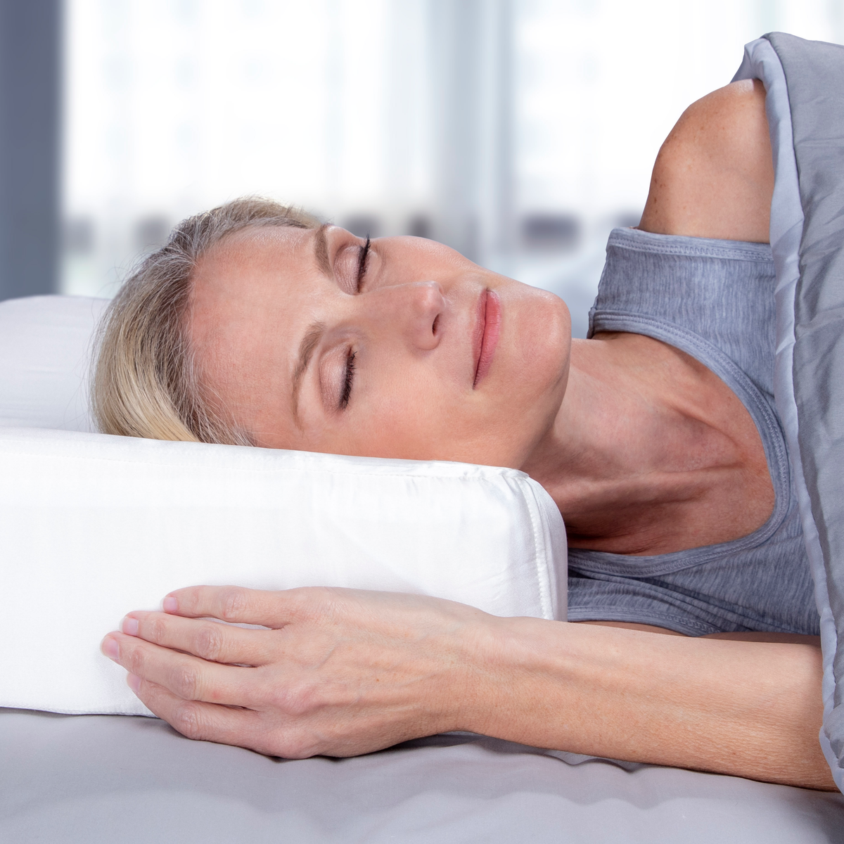Woman side sleeping on the enVy ergonomic pillow showing reduced facial compression and improved cervical alignment through OFF-Your-Face® support