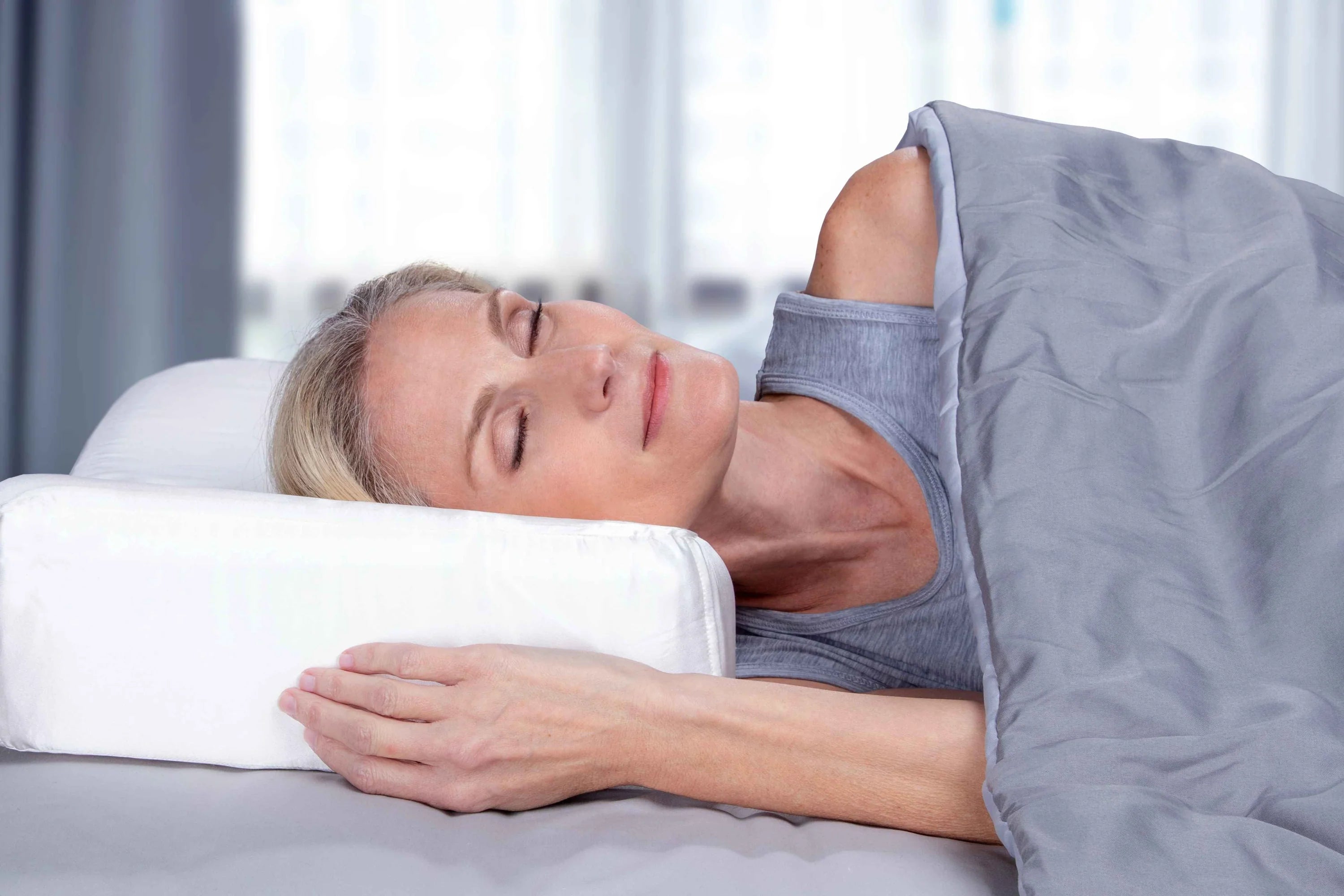 Woman side sleeping on the enVy ergonomic pillow showing reduced facial compression and improved cervical alignment through OFF-Your-Face® support